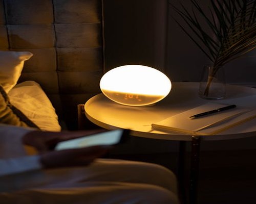An e-reader resting on a bedside table next to a small lamp